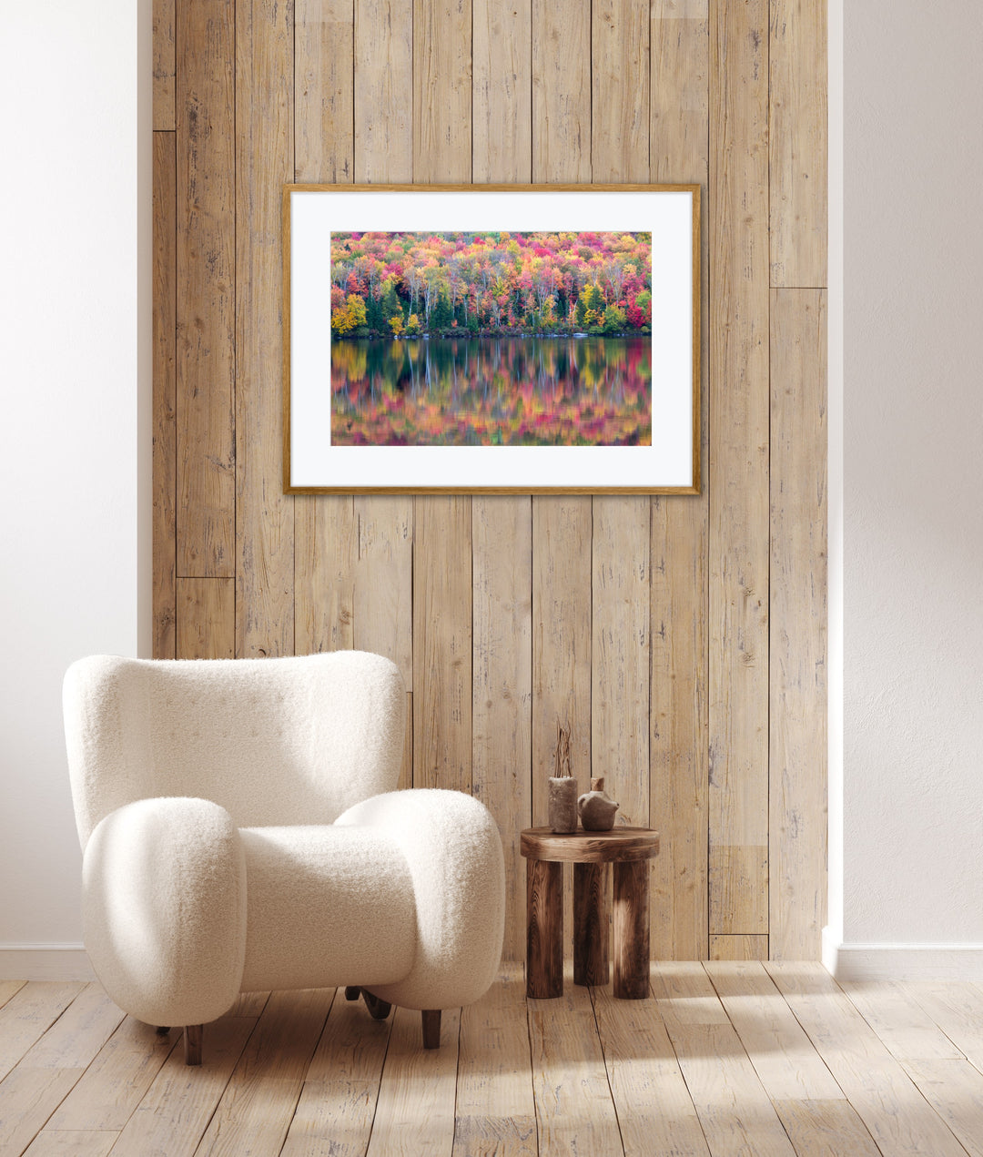 White armchair in a room with a framed picture of a colorful autumn landscape on a wooden wall.