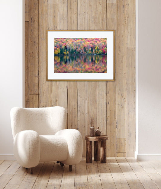 White armchair in a room with a framed picture of a colorful autumn landscape on a wooden wall.