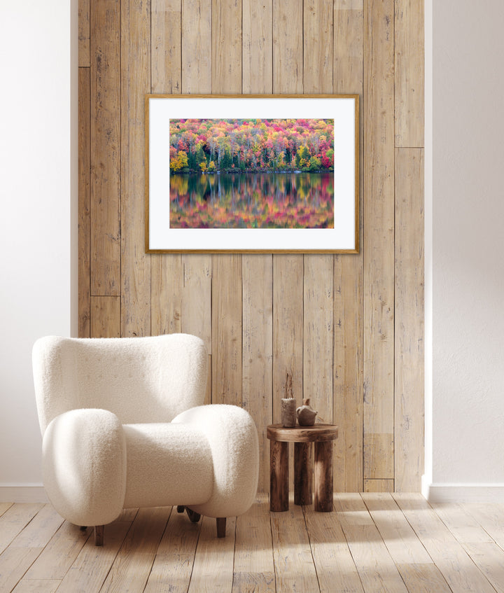 White armchair in a room with a framed picture of a colorful autumn landscape on a wooden wall.
